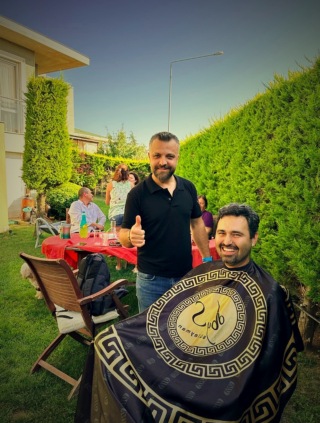 Bahçede Bay Süleyman pelerini giymiş gülümseyen müşteri ve berber